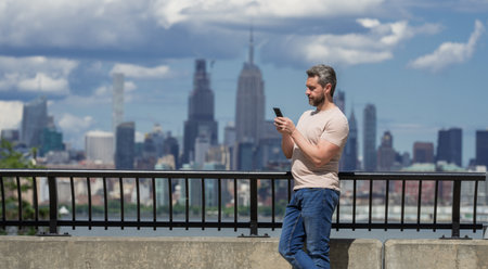 Mature Man talking at the phone in New York City. Man talking on the phone on NY. Male model in t-shirt talking on cell phone. Guy talking by mobile phone. Tourist in city street holding smartphone.の写真素材