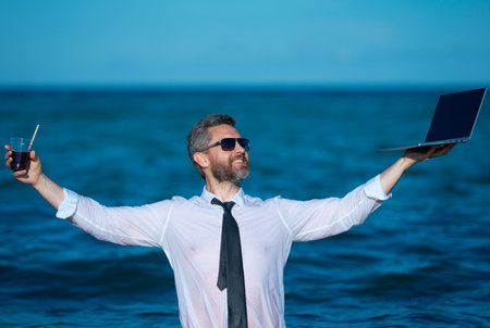 Fun business lifestyle. Freelance work, distance online work, e-working. Summer business. Business man in shirt remote working on laptop in sea water. Business man working online.の写真素材