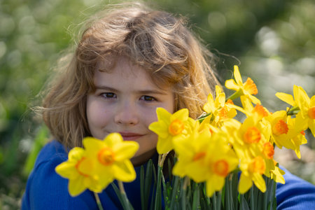 Little kid smelling spring narcissus flower outdoor. Child play in Spring garden. Kids face near Blooming cherry tree. Happy child during spring blossom.の写真素材