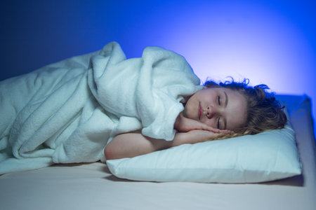 Child sleeping in a bed. Cute kid sleep. Kids pillow and blanket for sleeping. Little boy sleeps. Adorable kid sleeps in bed. Kid sleeping in dark bedroom. Child sleeping on a bed at home.の写真素材