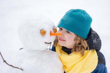 Kid play with snowman in winter. Snowman with a carrot nose on a winters day. Child making snowman....