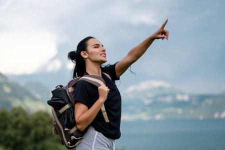 Woman tourist with backpack at the Switzerland Alps mountain lake pointing. Adventure, travel, tourism and hike people concept. The tourist girl with pointing finger. Hiker woman.の写真素材