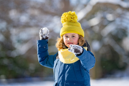 Kid playing with Snowball snow during snowfall. Snowball fight. Kid in a warm clothes, hat, hand gloves and scarf playing Snowball. Snowy winter day for kids. Child snowball fight in snow.の写真素材