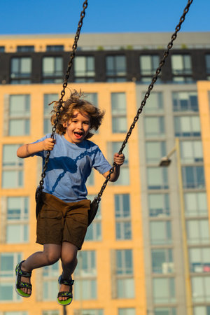Joyful kid swinging on a swing. Happiness children. Child having fun on a swing outdoor. Kid playing...