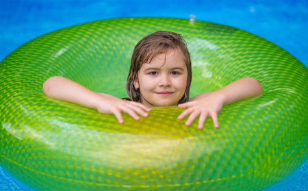 Kid playing in kids pool at home. Kids swim and splash in pool in garden backyard. Kids boy swim in inflatable circle pool on summer sunny day outdoors on home yard. Kids swimming pool at home.の写真素材