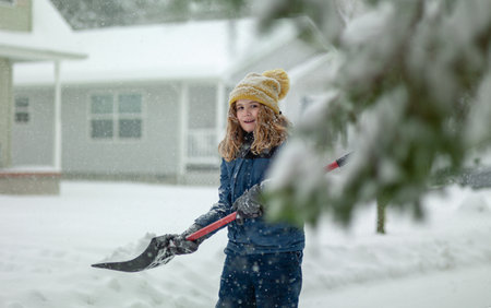 Child clearing sidewalks and shoveling snow. Child removing snow with shovel. Little helper. Winter kids fun outdoor. Child with a shovel is clearing snow after strong snowstorm. Winter cold season.の写真素材