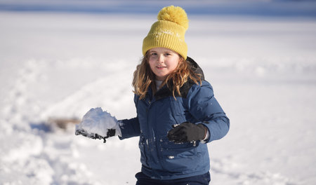 Child Winter playing. Kid boy play in the snow with a winter hat. Happy kid in warm clothes enjoying...