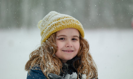Winter kids portrait in snow. Kid winter face in snow. Happy Winter Children Holidays. Emotional Smiling Child Having Fun Playing with Snowflakes in Snow Park. Snow Falling in Winter Vacations.の写真素材