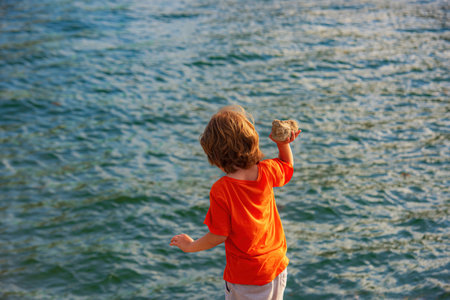 Child boy on lake throw a stone in water. Lake landscape background.の写真素材