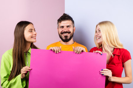Group of friends showing board. People hold banner mockup, copy space. Team of 3 friends holding empty billboards. Funny three people holding a blank sign. Group displaying blank billboard.の写真素材