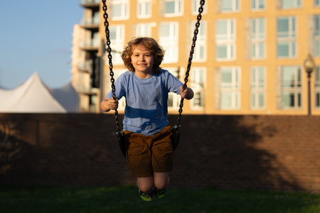 Child swing on city playground. Kids play public city park playground. Kid swinging. Summer activity for children. Kid on chain swing. Carefree and freedom childhood. Child swinging.の写真素材