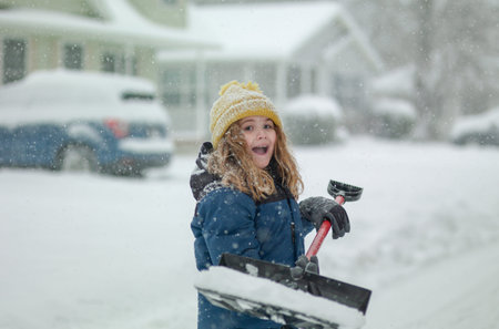 Child clearing sidewalks and shoveling snow. Child removing snow with shovel. Little helper. Winter...