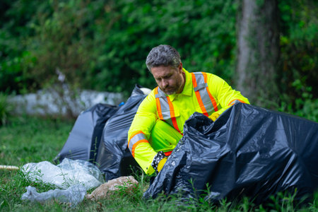 Volunteer in rubber gloves with trash bag clean up garbage on forest outdoor. Eco, environment...