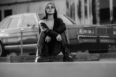 Fashion woman street. Fashion woman sitting outdoor. Fashionable brunette in black jacket bandana and sunglasses in urban style. Lifestyle of female hipster.の写真素材