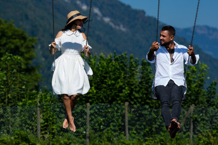 Man and woman sitting together on swing and enjoying summer. Couple lovers enjoy summer vacation on green nature. Couple in love siiting on the swing and relax.の写真素材