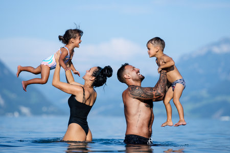 Happy family on summer. Father and mother play with son and daughter. Loving family. Parents lift children up. Vacation with kids. Caring family. Parents throw kids up and catch them. Family travel.の写真素材