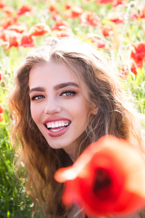 Spring woman face in blooming meadow. Beautiful girl face in summer poppies field. Romantic woman face in a field flowers. Tender beauty young woman on spring meadow. Beauty woman face on nature.の写真素材