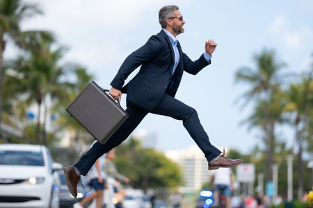 Busy rich businessman running to a meeting. Businessman run on road. Business man in a suit run to work. Business man jump and run outdoor. Businessman running to meet. Business man run in hurry.の写真素材