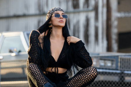 Fashion street. Fashion woman sitting outdoor. Fashionable brunette in black jacket bandana and...
