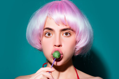 Lollypop in woman's mouth. Girl enjoys sweets. Model licks a candy treat. Beautiful woman with a lollipop. Lips and playful licking. Model sucking a lollypop.の写真素材