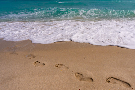 Turquoise sea water wave motion. Foot steps on sand. Calm sea. Seaside resort. Bright sky and waves on beach. Beautiful foamy shoreline. Sea background. Blue ocean. Sandy ocean beach. Sea waves.の写真素材