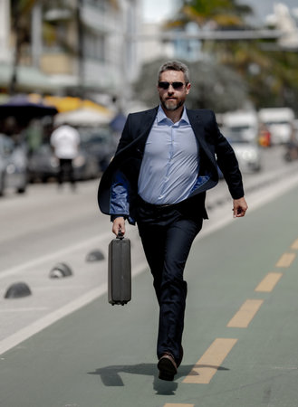 Business man running in street. Busy entrepreneur running to work. Hurry man in suit running late outdoors. Confident businessman running towards success. Office worker in hurry to meet a deadline.の写真素材