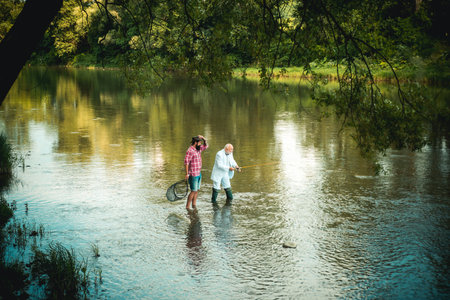 Two men friends fisherman fishing on river. Old father and son with rod fishing at riverside. Recreational activity.の写真素材