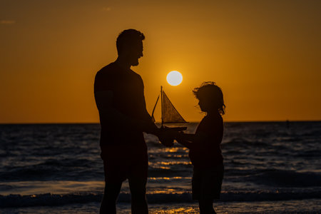 Father and son kid playing with toy boat ship. Travel and adventure concept. Father and son feeling adventurous while cruising. Father and son on summer sunset beach. Men family. Fathers day.の写真素材