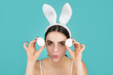 Cheerful young woman wearing Easter bunny ears holding decorative colored eggs on studio background with copy space.の写真素材