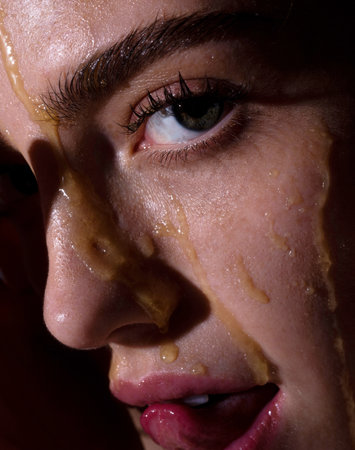 Sensual young woman face with honey drop close up. Model with honey drip on face.の写真素材