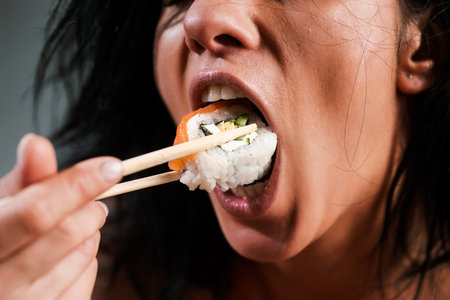 Sushi in woman mouth. Woman eating sushi with chopsticks. Model eat sashimi. Sensual bite of sushi. Female tasting nigiri. Lunch at Japanese restaurant. Desire for delicious sushi. Asian food.の写真素材