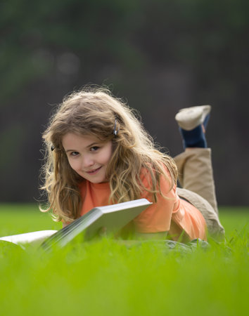 Child reading a book in the grass. Kid enjoying a book story outdoors. Child studying with book in the meadow on a sunny day. Learning in nature. Schoolboy reading book in the park. Outdoor learning.の写真素材