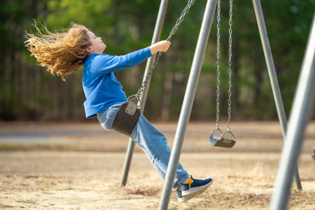 Playful child on swing in park. Little kid with blond hair on a swing. Smiling happy kid on swing. Happy childhood moment. Child playing outdoors. Kid having fun on swing. Outdoor play for kids.の写真素材