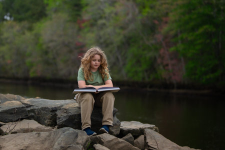 Kid reading book in outdoors. Child read story outdoors. Portrait of teen reading in nature. Boy with book studying on nature. Kid reading book. Child reading book in peaceful park.の写真素材