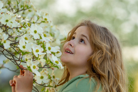 Spring flowers around child. Kid in blooming spring garden. Child face close to spring flowers....