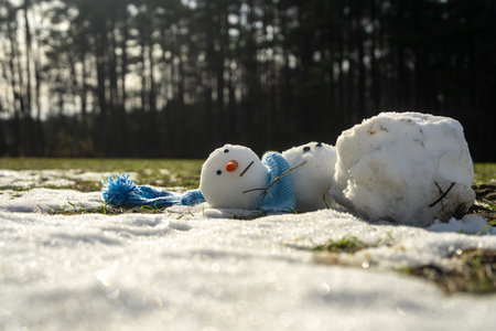 Snowman melting in warm winter or spring weather. Melted snowman as a symbol of warm winter spring. Winter and spring seasons change. Melting snowman with puddles around it. From winter to spring.の写真素材