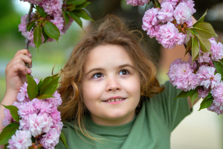 Spring flowers around child face. Kid in blooming spring garden. Child face close to spring flowers. Dreamy kid face in spring orchard.の写真素材