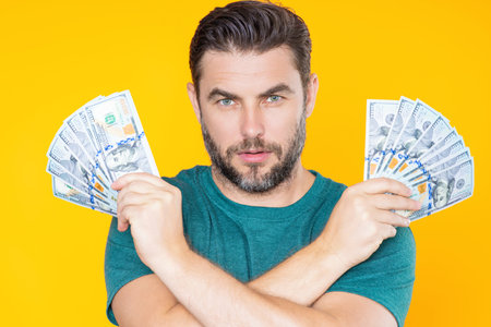 Man holding cash money in dollar banknotes on isolated yellow background. Studio portrait of business man with bunch of dollar banknotes. Dollar money concept. Career wealth business. Cash dollar.の写真素材