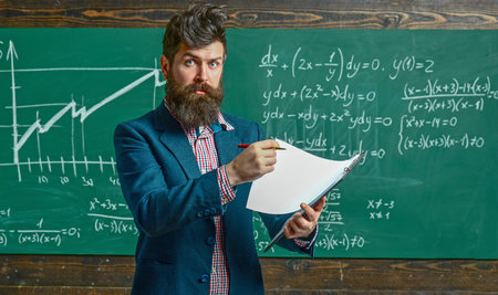 Teacher explains math in class. Professor in classroom on math lesson. School teacher writes math formula. Funny teacher. Professor teaching lesson in classroom. Teacher explains math. Teachers day.の写真素材