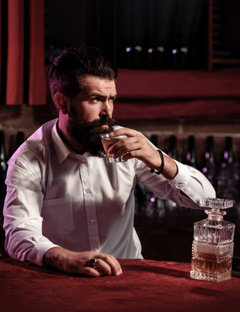 Man drinking whiskey at bar. Handsome man enjoying a drink. Whiskey moment with serious face. Man holding classic whiskey glass. Man tasting aged whiskey alone.の写真素材