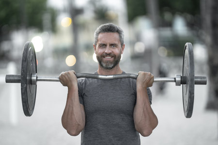 40s man doing fitness exercises. Healthy workout. Miami beach fitness model with barbell. Healthy lifestyle barbell training. Mature man exercising with barbell outdoors. Man lifting barbell.の写真素材