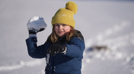 Kids Winter playing. Kid boy play in the snow with a winter hat. Happy kid in warm clothes enjoying snow falling. Child play with snow outdoors during first snowfall. Winter activities for kids.の写真素材