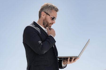 Business man using laptop outdoors. Mature businessman with laptop. Confident business man with laptop. Business online. businessman checking data on laptop outside. Business man in suit work online.の写真素材