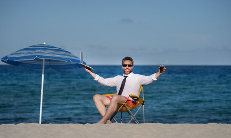 Remote online working on summer sea beach. Business man with laptop during tropical beach vacation. Leisure weekend and remote freelance work. Comic businessman rest on sea beach.の写真素材