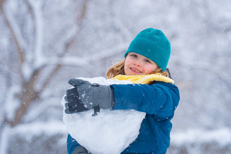 Funny Kid make snowballs for snowman in winter. Kid play in snow. Active winter outdoor games. Boy...