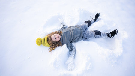 Child making a snow angel. Happy kid lying in the snow. Kid angel in snow. Winter kids with snowy...