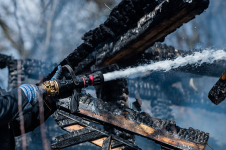 Firefighter put out a fire. Brave firefighter battling house blaze. Firemen in uniform near burning home. Firefighter uses hose to control fire. Firefighting concept. Firefighter in helmet on flame.の写真素材