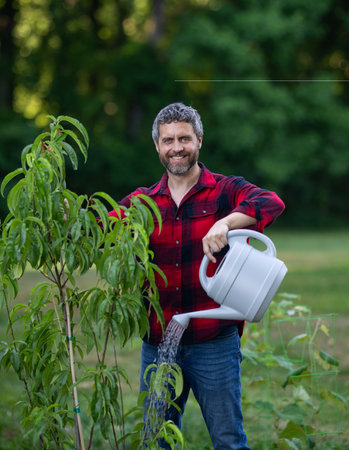 Gardener growing plants in the garden. Gardener plant tree in home yard. Gardener planting tree. Gardening with watering can. Home garden. Yard with fruit tree. Mature gardener planting tree.の写真素材