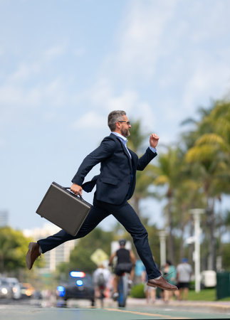 Business jump. Funny business man jumping in the street. Businessman in a suit running late and jump. Busy business man in jump motion. Confident businessman office worker jump up with excitement.の写真素材