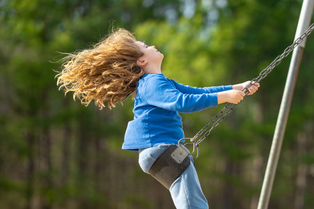 Child enjoying a fun ride on swing. Happy kid on playground. Carefree kid swinging outdoors. Happy children play outside. Blonde kid swinging with excitement. Playful kid outdoor. Fun kids face.の写真素材